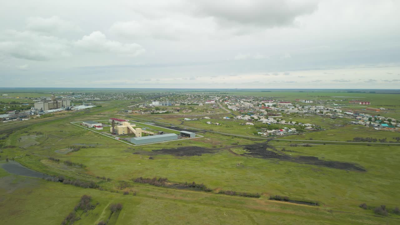 Aerial View of a Small Town and Industrial Buildings in a Green Rural Landscape Under a Cloudy Sky