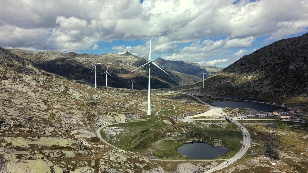 Movimento aéreo de câmera para frente passando por turbinas eólicas na paisagem rochosa dos Alpes Suíços