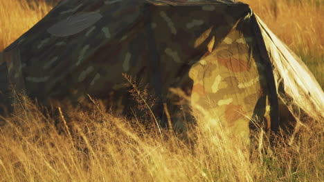 camouflage tent in grassy field with front flap blowing in the wind