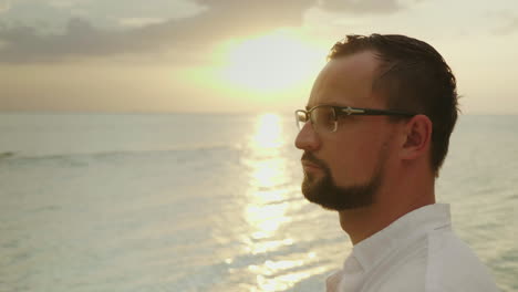 Retrato-De-Un-Joven-En-Una-Playa-Tropical-Con-Una-Camisa-Fácil,-Sonríe-Y-Mira-A-La-Cámara-Wea