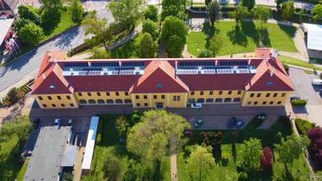 Drone-descends-on-yellow-building-with-red-roof-in-Kapuvar,-Hungary