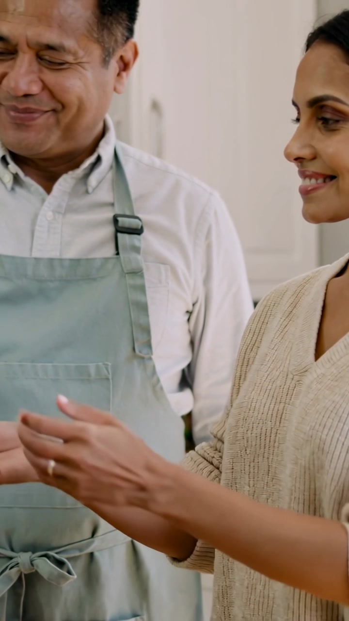 Vertical video: Receiving woman taking magenta drink from man in green apron in kitchen to share