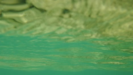 Una-Toma-Del-Techo-Del-Océano-Justo-Debajo-Mirando-Hacia-El-Cielo-Con-Olas-Suaves-Y-Un-Reflejo-Verde-Brillante-Del-Arrecife-Y-Los-Corales-Debajo-En-El-Mar-De-Andamán