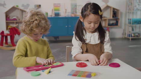 little girl playing with play dough and little boy playing with a shape sorter while sitting at desk in a montessori school