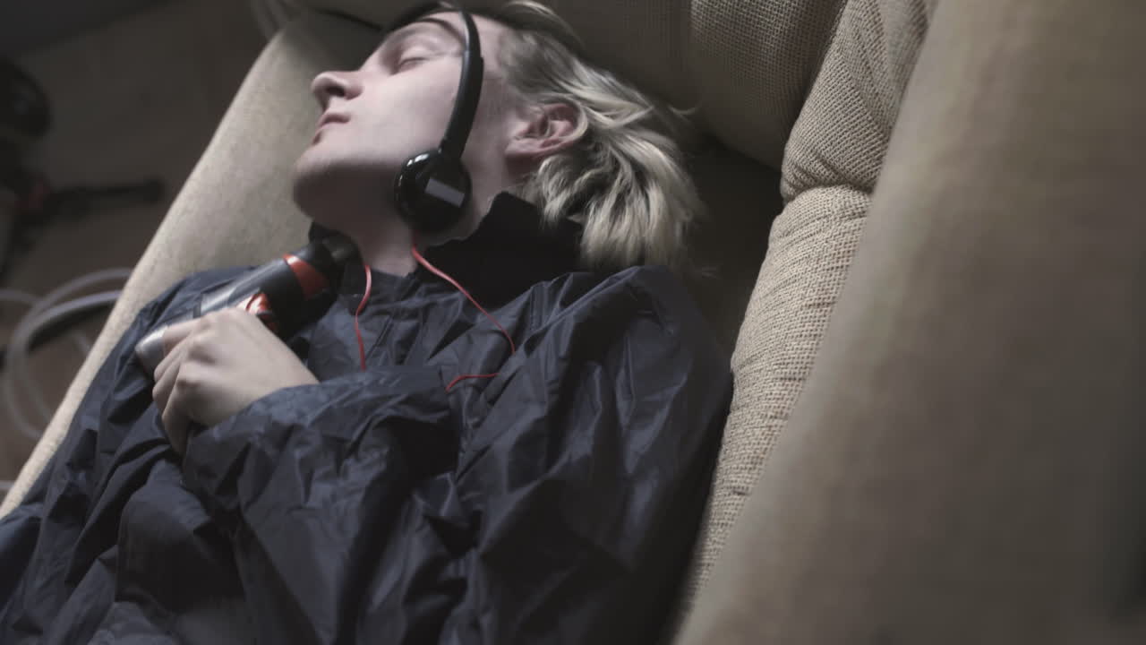 젊은이가 음악을 듣고 도구와 함께 소파에서 잠을 자고 있습니다.