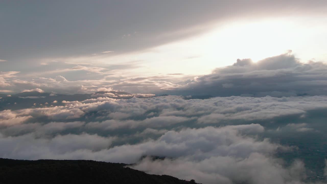 High flight above mountains and valleys covered with white carpet clouds with bright white sun in background, aerial overhead sideways
