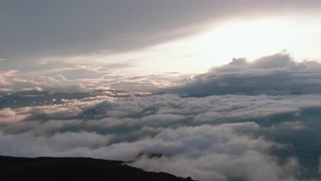 high flight above mountains and valleys covered with white carpet clouds with bright white sun in background, aerial overhead sideways