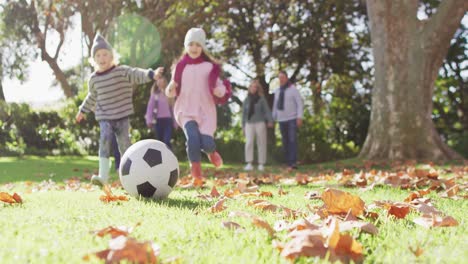 Video-of-happy-caucasian-brother-and-sister-kicking-football-in-autumn-garden,-family-walking-behind