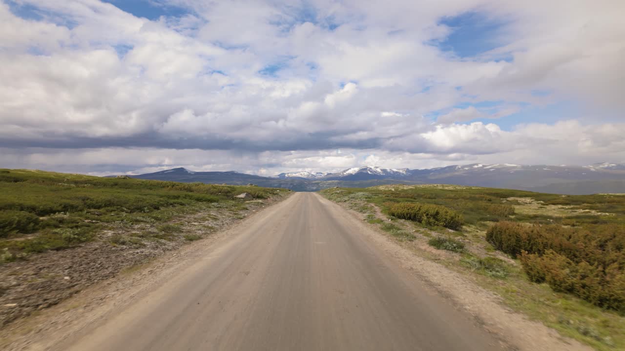 Uma longa estrada de cascalho se estende por terrenos abertos das montanhas em direção a montanhas distantes ao longo de Slådalsvegen, com vistas de Dovrefjell, Noruega - Close up