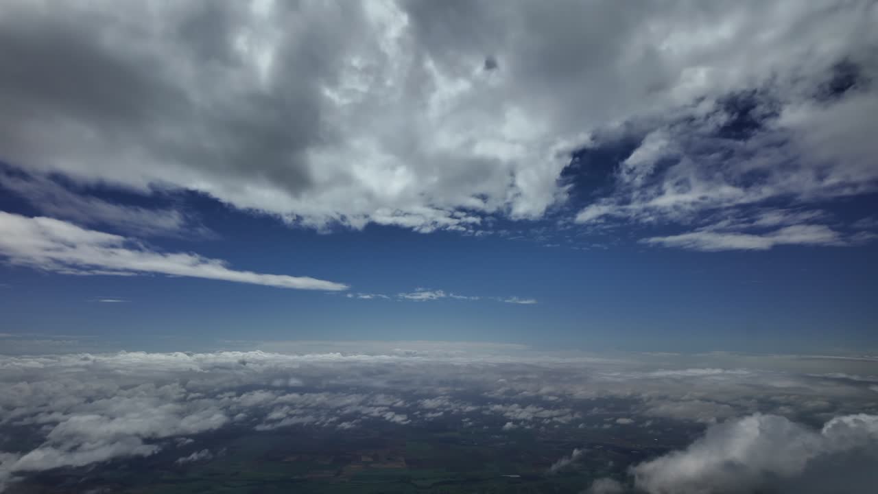 an immersive aerial view of a peaceful sky with some fluffy white clouds under a blue sky. Aerial footage taken from a jet cockpit.