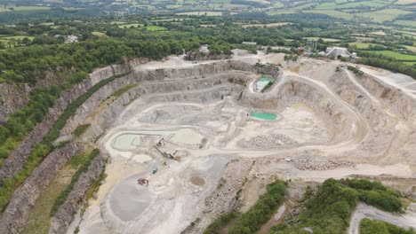 aerial view of a large open-pit quarry with heavy machinery and water bodies
