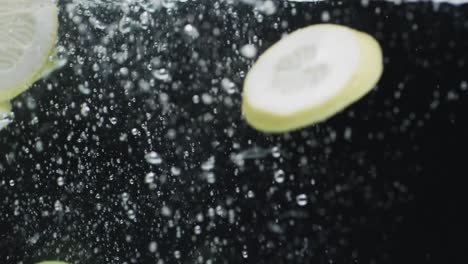 Video-Von-Limetten--Und-Zitronenscheiben,-Die-Ins-Wasser-Fallen,-Mit-Kopierraum-Auf-Schwarzem-Hintergrund
