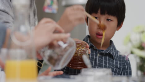 아시아 가족이 아침 식사를 하고 있습니다. 어머니는 작은 소년을 위해 팬케이크에  ⁇ 을  ⁇ 고 있습니다. 어머니는 아이들을 위해 집에서 만든 식사를 준비하고 있습니다.