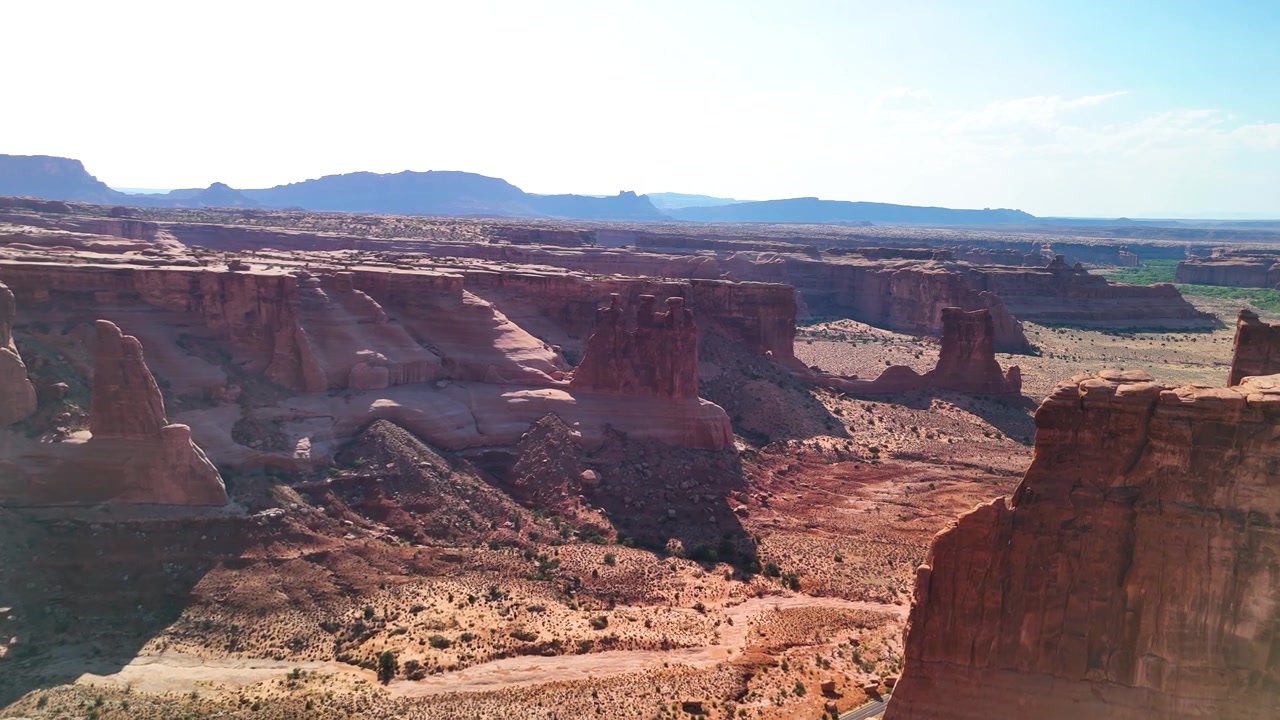 Splendido filmato stock dell'Arches National Park USA durante un pomeriggio luminoso. La luce solare brillante illumina le maestose strutture di arenaria rossa e il paesaggio desertico sotto un cielo azzurro e limpido