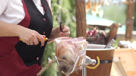 close up of female slicing dried prosciutto with knife outdoors, natural light, slow motion