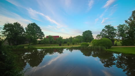 Timelapse-De-Una-Puesta-De-Sol-Pastel-En-El-Campo-Con-Un-Lago-Y-Una-Cabaña