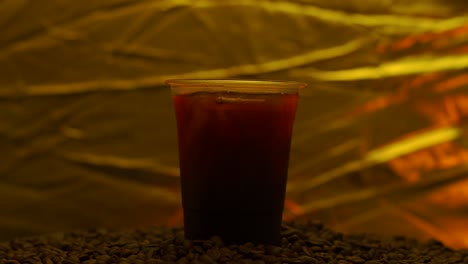 black coffee iced in disposable plastic cup rotated against gold background.