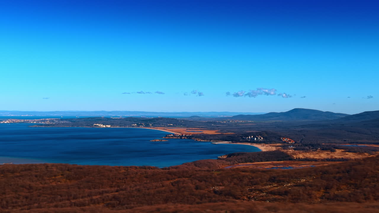 Veduta aerea panoramica di una baia di mare blu e di una costa autunnale. Ampia inquadratura dall'alto di un paesaggio costiero con acqua blu, vegetazione secca marrone, colline e cielo sereno.