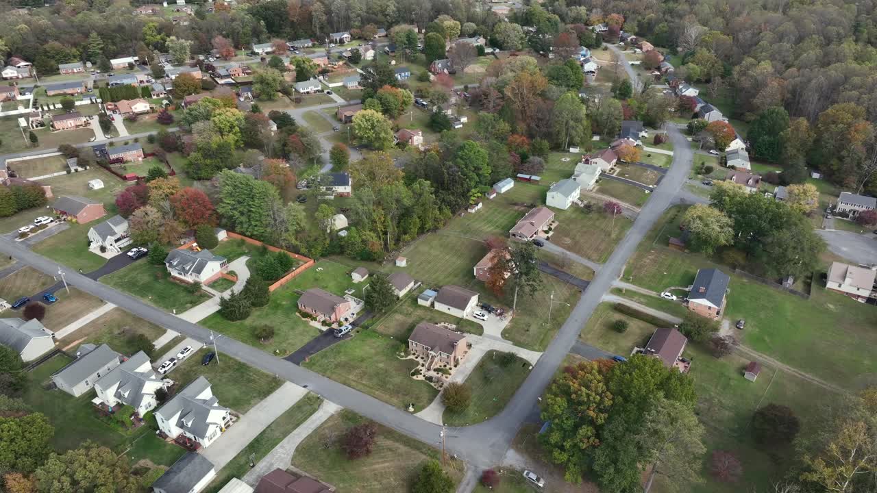 Aerial drone view of American suburban neighborhood with vibrant autumn foliage, quiet streets, spacious yards and surrounding woodlands under clear daylight. Top down. Virginia, USA