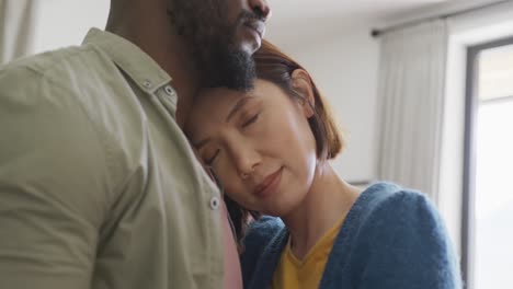 video of happy diverse couple embracing with eyes closed and smiling at each other at home