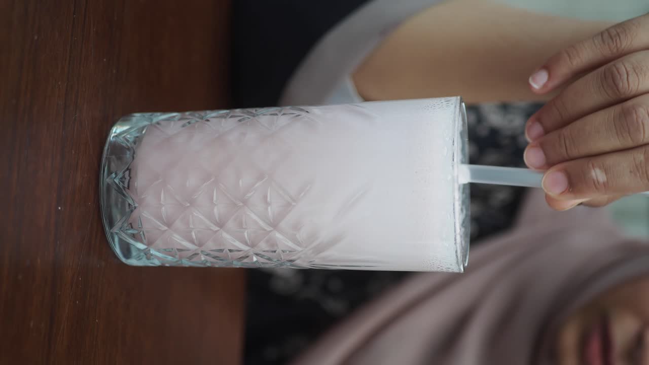 Close-up of a pink frothy drink in a textured glass with a straw