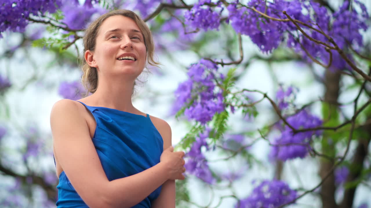 Caucasian woman in blue dress posing, tree with pink flowers in Barcelona, Spain