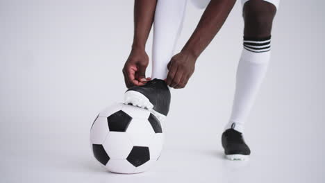 Close-up-of-black-african-male-soccer-player-tying-shoelace-on-studio-slow-motion.-Footballer-tying-his-shoe.-Low-section.-tying-football-boots-preparing-in-white-background