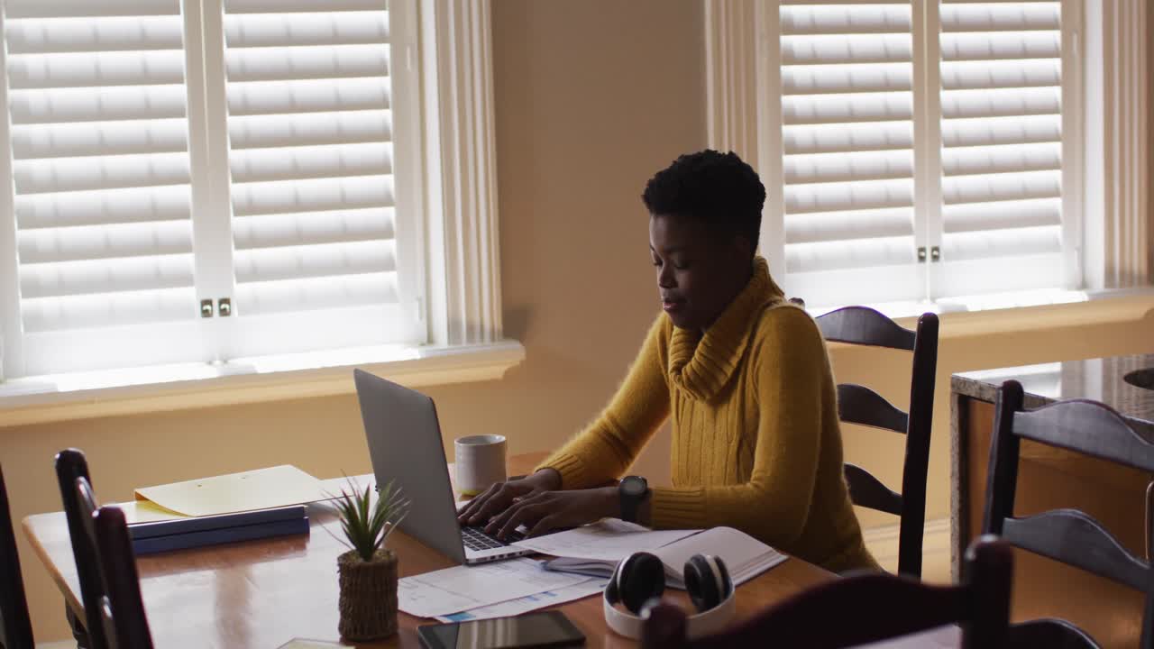 African american woman using laptop and reading documents while working from home