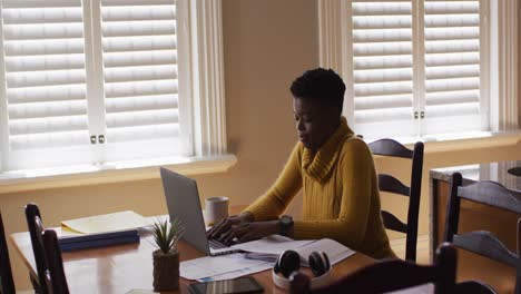 african american woman using laptop and reading documents while working from home