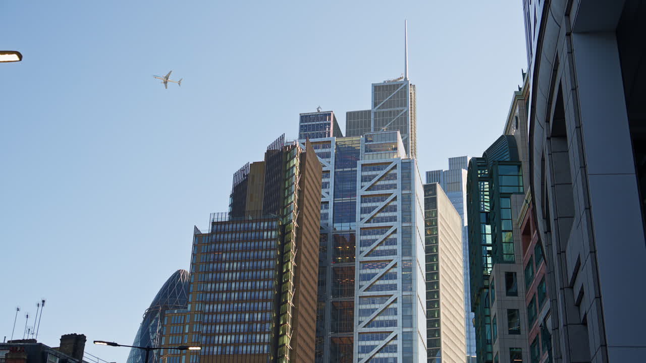 Skyline of London featuring the Gherkin, Leadenhall Building, and other modern skyscrapers under clear sky. Airplane passing by