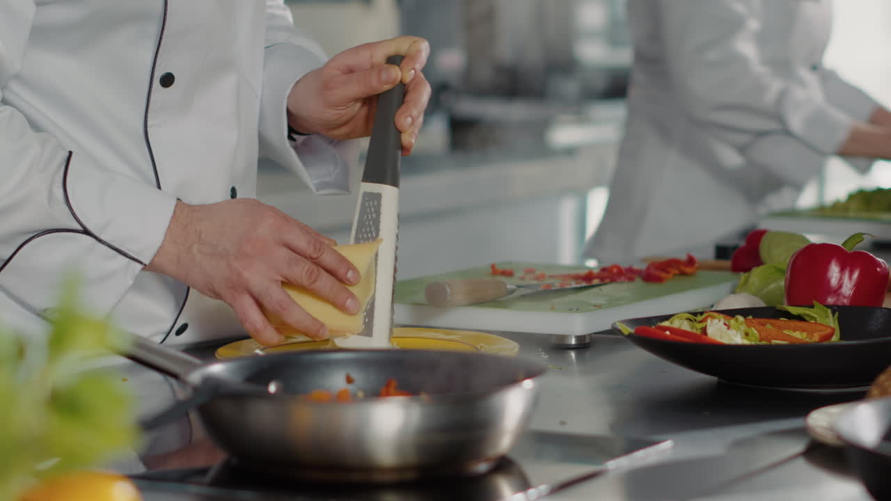 Professional chef using grater to add shredded cheese on dish