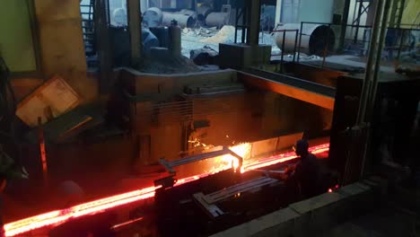 worker in steel fabrication plant at red hot molten metal forming billets station, during casting.