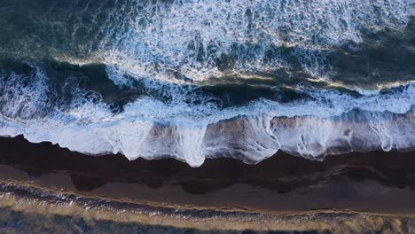 drone view of south coast ocean with black sand and waves - aerial ascending