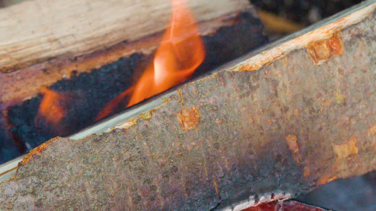 Macro view of burning wood, glowing embers, and smoke rising in natural daylight