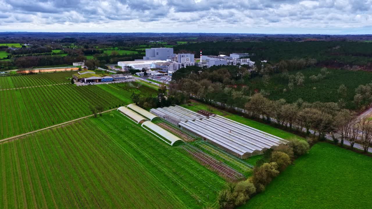 Panoramische dronebeelden tonen een groen landschap met kassen en een industrieel gebouw in de verte.