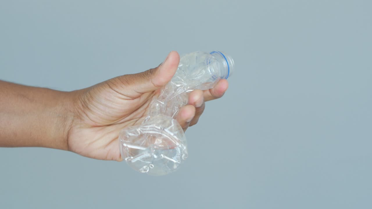 mano con una botella de plástico triturada