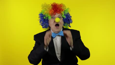 senior old woman clown in colorful wig looks surprised shocked. amazement