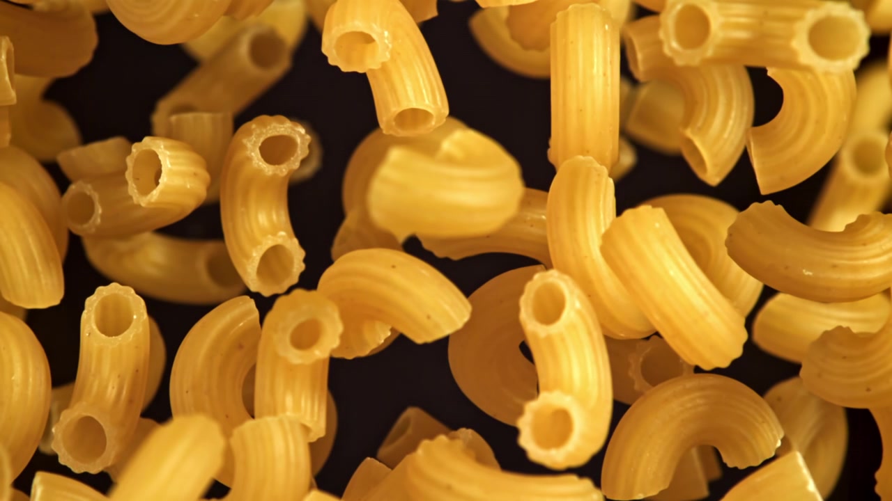 Maccheroni secchi che cadono al rallentatore su uno sfondo scuro