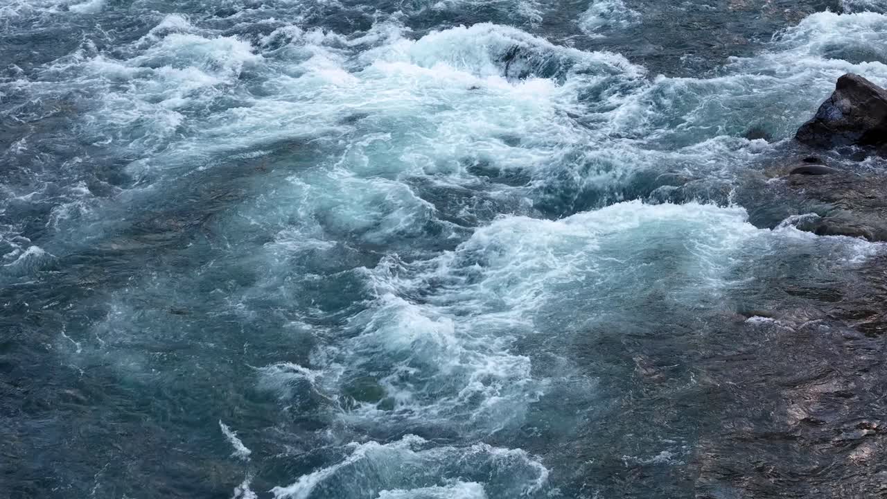 Vista aérea de rápidos turbulentos de águas brancas agitando-se e espumando em um rio de montanha turquesa com rochas expostas em Montana, perto do Parque Nacional Glacier