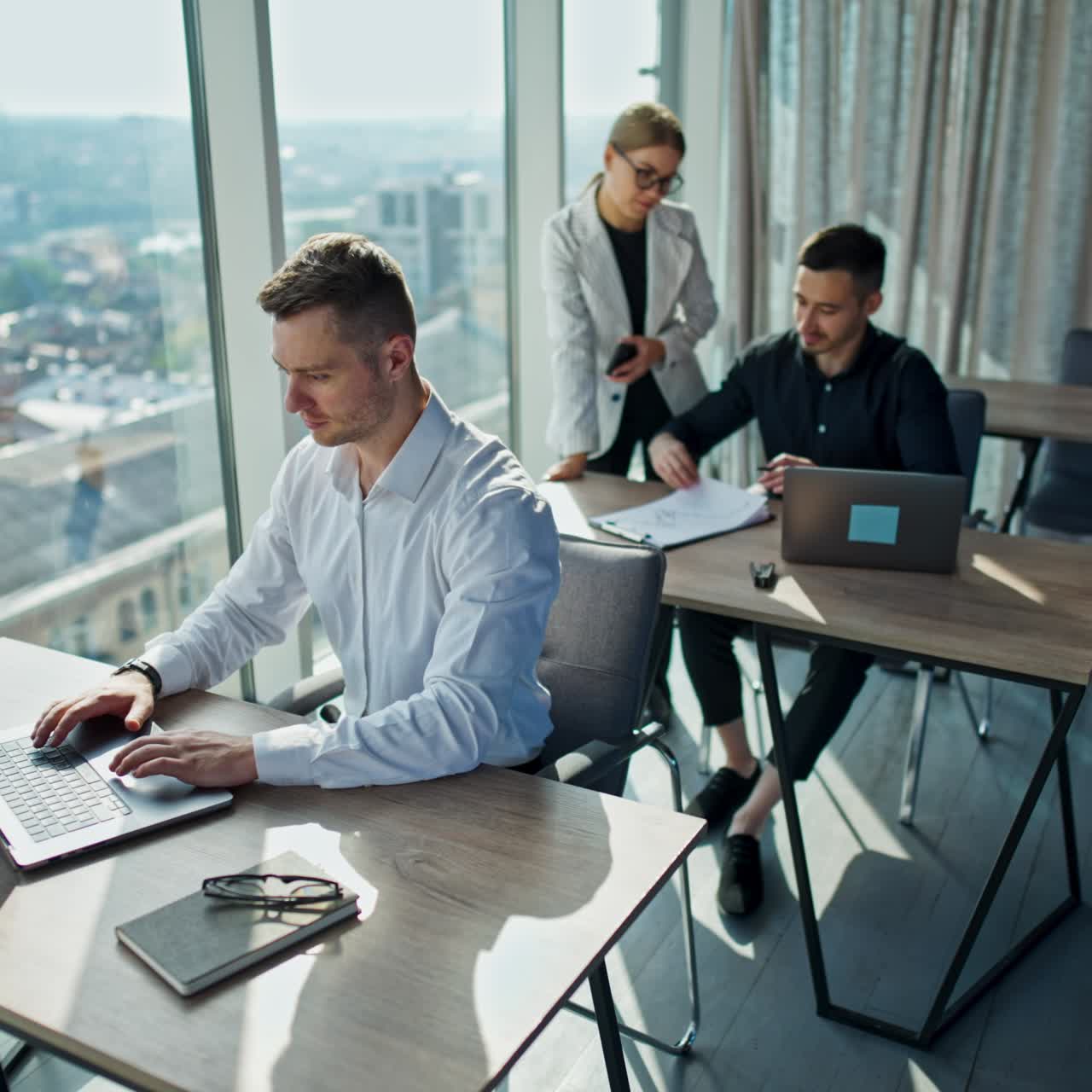 Impiegati d'ufficio che lavorano in un ufficio moderno e soleggiato. Uomini seduti alla scrivania davanti ai computer portatili. Donna in giacca bianca in piedi vicino al collega in camicia nera