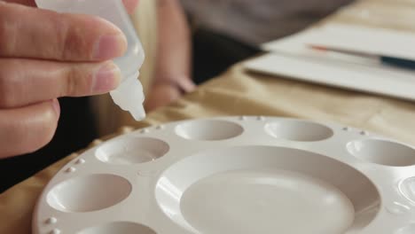 Closeup-shot-of-hand-squeezing-clear-liquid-like-water-into-well-of-white-paint-palette