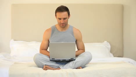 hombre bonito trabajando en una computadora portátil sentado en la cama