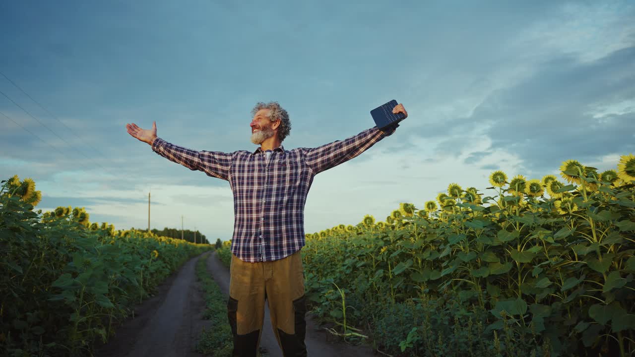 Happy Farmer in a Sunflower Field with Tablet