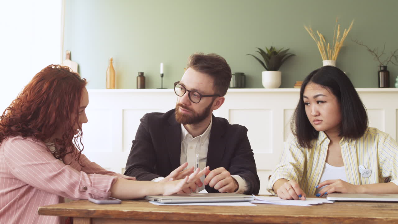 팀 회의 중에 테이블에 앉아 있는 동안 두 동료에게 무언가를 설명하는 젊은 전문 여성