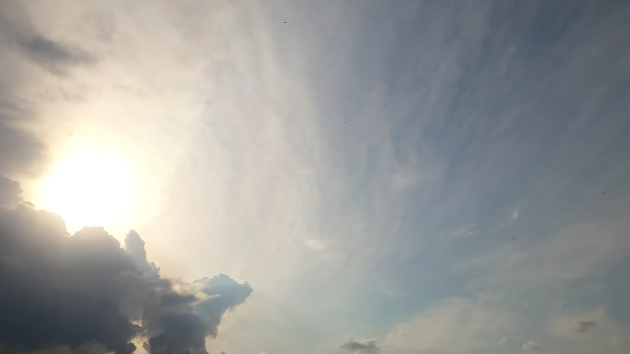 Cumulus and stratus clouds quickly changing shapes in the wind. Low angle view at the sky with transforming cloudscape covering the sun. Timelapse