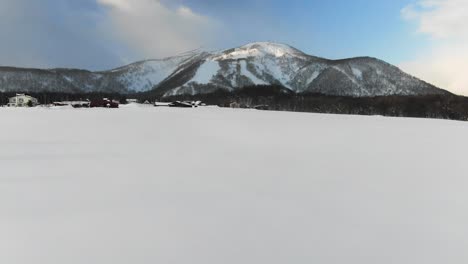 4K-drone-footage-of-snowy-field-in-rural-village-pans-up-to-reveal-Niseko-ski-resort-in-Japan