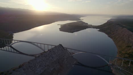 Bright-sunlight-shines-in-sky-with-aerial-view-of-Krk-Bridge,-Croatia