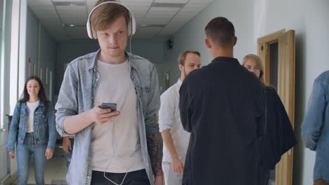 an introverted man walks in a crowd of college students and listens to music. concentrate on your thoughts. modern student in white headphones in the hall of the university