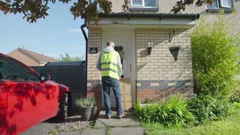 Delivery-driver-wearing-high-vis-jacket-arrives-at-a-house-with-box