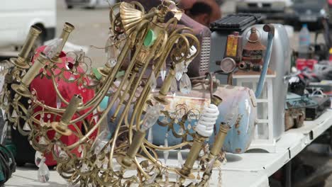 a vintage, gold-colored metallic chandelier and other antique items are elegantly displayed at the flea market, attracting attention with its timeless charm and character.